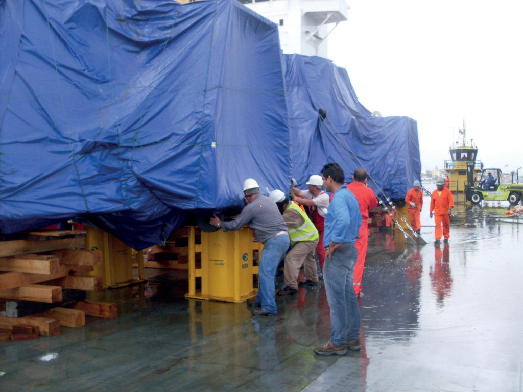 Equipe posicionando carga de grande porte coberta por lona em um porto